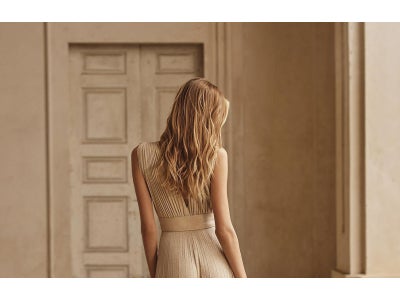 Damigella di spalle che indossa un vestito da cerimonia beige con scollo a V sulla schiena. 