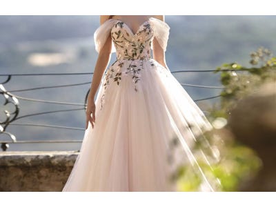 Modella con abito da sposa romantico rosa a principessa con scollo a cuore, spalle scoperte e dettagli floreali sul corpetto.