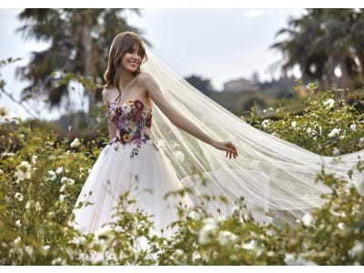 Une belle jeune femme vêtue d’une magnifique robe de mariée champêtre rehaussée de fleurs en dentelle colorées sur le buste.