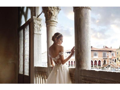 Modella di spalle che si affaccia da un porticato e si guarda la mano mentre indossa un abito da sposa con maniche pendenti.