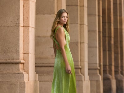 Modella di profilo seduta sui talloni che indossa una vestito da cerimonia lilla corto con corpetto e strascico in tulle.