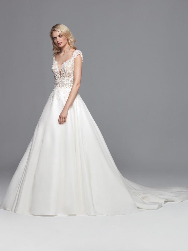 Romantic mermaid wedding dress of light pink Chantilly lace with plunging V-neck that continues on the sleeves. The keyhole opening in back and the tulle overskirt add romanticism to this dreamy dress.