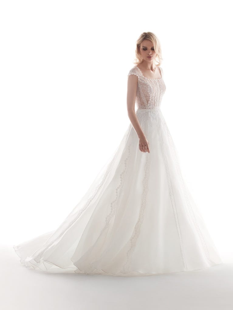 Romantic mermaid wedding dress of light pink Chantilly lace with plunging V-neck that continues on the sleeves. The keyhole opening in back and the tulle overskirt add romanticism to this dreamy dress.