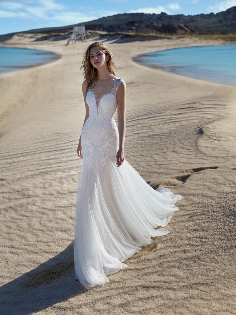 Flared wedding dress with crepe skirt and a tulle cape embroidered with silver beads. The three-dimensional flowers and minimalist, geometric superimpositions of fabrics create a contemporary, unique look for brides who want to surprise.