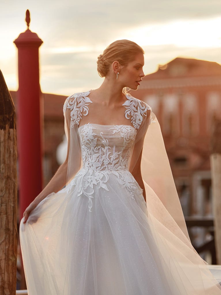 Flared wedding dress with voluminous yet lightweight tulle skirt with lace embroidered with floral motifs. For brides who dream of a romantic, feminine dress to say “I do.”