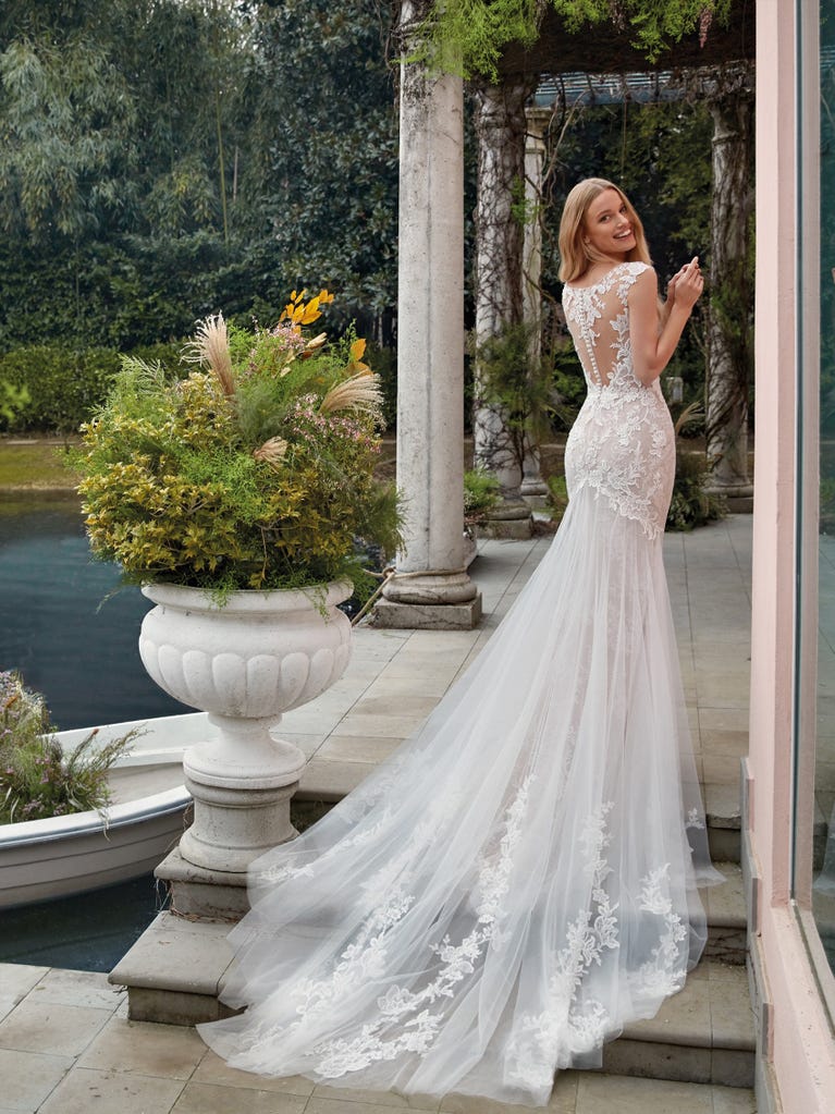 Flared wedding dress with crepe skirt and a tulle cape embroidered with silver beads. The three-dimensional flowers and minimalist, geometric superimpositions of fabrics create a contemporary, unique look for brides who want to surprise.