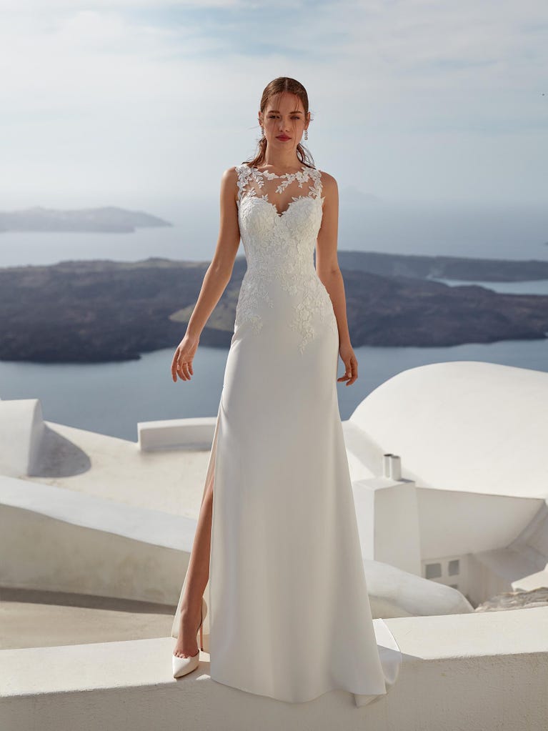 Flared wedding dress with crepe skirt and a tulle cape embroidered with silver beads. The three-dimensional flowers and minimalist, geometric superimpositions of fabrics create a contemporary, unique look for brides who want to surprise.
