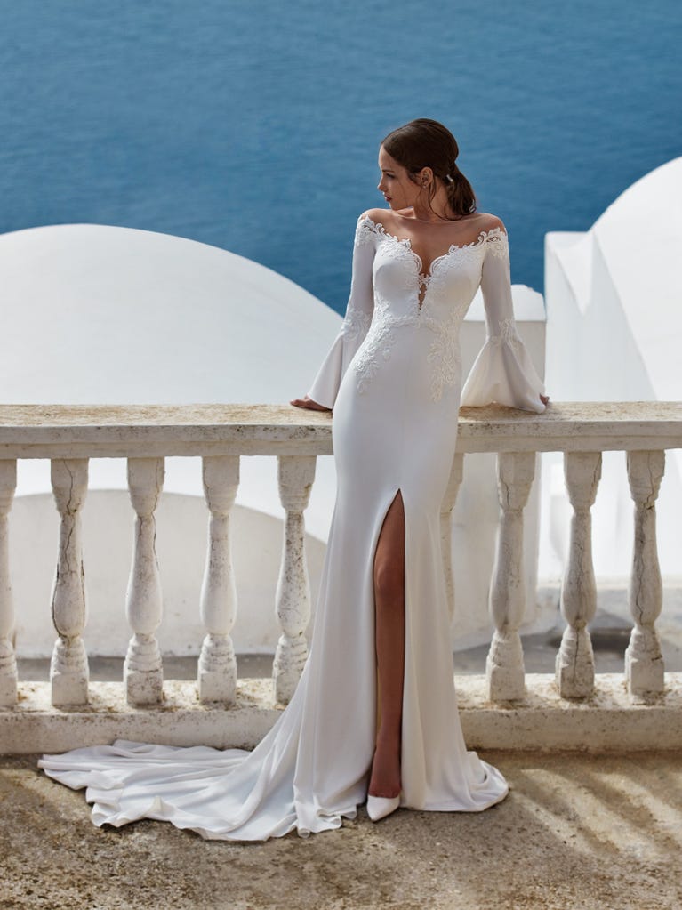 Flared wedding dress with crepe skirt and a tulle cape embroidered with silver beads. The three-dimensional flowers and minimalist, geometric superimpositions of fabrics create a contemporary, unique look for brides who want to surprise.