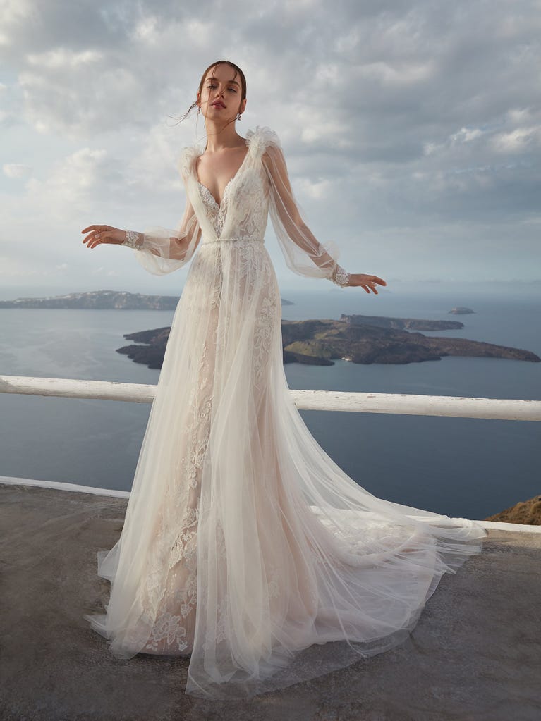 Flared wedding dress with crepe skirt and a tulle cape embroidered with silver beads. The three-dimensional flowers and minimalist, geometric superimpositions of fabrics create a contemporary, unique look for brides who want to surprise.