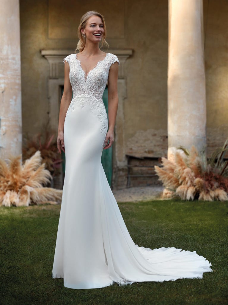 Flared wedding dress with crepe skirt and a tulle cape embroidered with silver beads. The three-dimensional flowers and minimalist, geometric superimpositions of fabrics create a contemporary, unique look for brides who want to surprise.