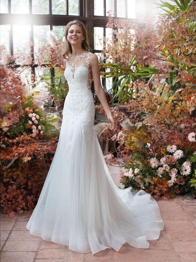 Flared wedding dress with crepe skirt and a tulle cape embroidered with silver beads. The three-dimensional flowers and minimalist, geometric superimpositions of fabrics create a contemporary, unique look for brides who want to surprise.