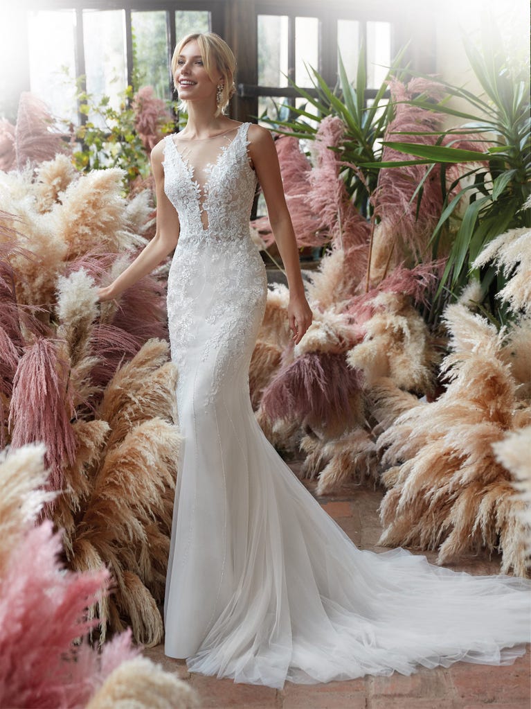 Flared wedding dress with crepe skirt and a tulle cape embroidered with silver beads. The three-dimensional flowers and minimalist, geometric superimpositions of fabrics create a contemporary, unique look for brides who want to surprise.