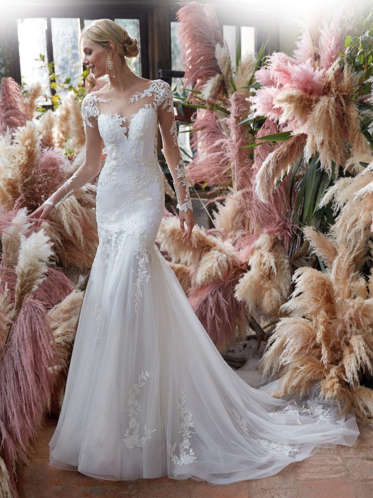 Flared wedding dress with crepe skirt and a tulle cape embroidered with silver beads. The three-dimensional flowers and minimalist, geometric superimpositions of fabrics create a contemporary, unique look for brides who want to surprise.