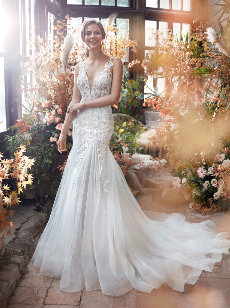 Flared wedding dress with crepe skirt and a tulle cape embroidered with silver beads. The three-dimensional flowers and minimalist, geometric superimpositions of fabrics create a contemporary, unique look for brides who want to surprise.