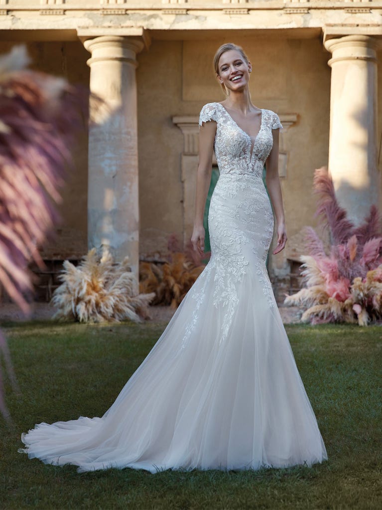 Flared wedding dress with crepe skirt and a tulle cape embroidered with silver beads. The three-dimensional flowers and minimalist, geometric superimpositions of fabrics create a contemporary, unique look for brides who want to surprise.