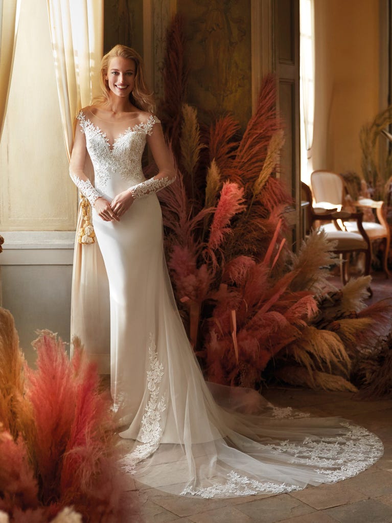 Flared wedding dress with crepe skirt and a tulle cape embroidered with silver beads. The three-dimensional flowers and minimalist, geometric superimpositions of fabrics create a contemporary, unique look for brides who want to surprise.