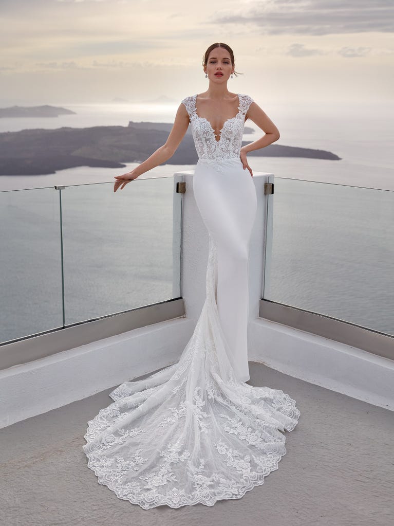 Flared wedding dress with crepe skirt and a tulle cape embroidered with silver beads. The three-dimensional flowers and minimalist, geometric superimpositions of fabrics create a contemporary, unique look for brides who want to surprise.