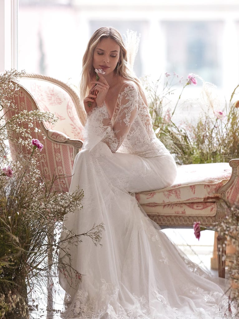 Flared wedding dress with crepe skirt and a tulle cape embroidered with silver beads. The three-dimensional flowers and minimalist, geometric superimpositions of fabrics create a contemporary, unique look for brides who want to surprise.
