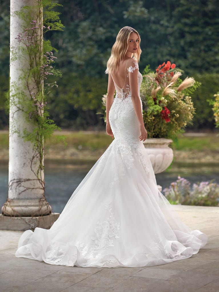 Flared wedding dress with crepe skirt and a tulle cape embroidered with silver beads. The three-dimensional flowers and minimalist, geometric superimpositions of fabrics create a contemporary, unique look for brides who want to surprise.