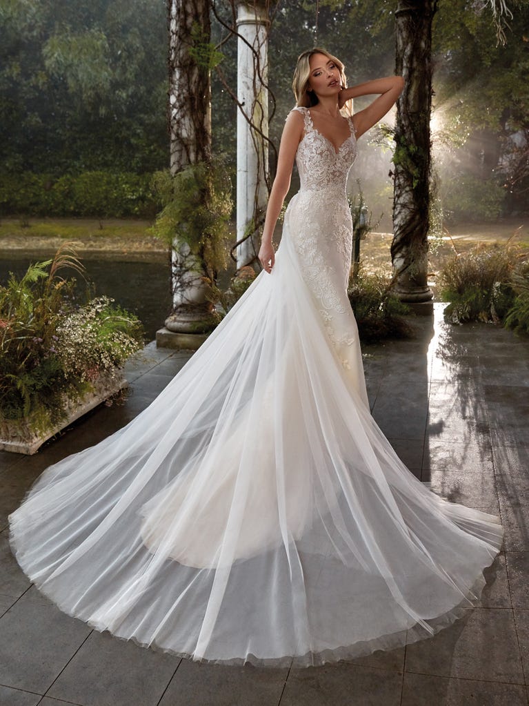 Flared wedding dress with crepe skirt and a tulle cape embroidered with silver beads. The three-dimensional flowers and minimalist, geometric superimpositions of fabrics create a contemporary, unique look for brides who want to surprise.