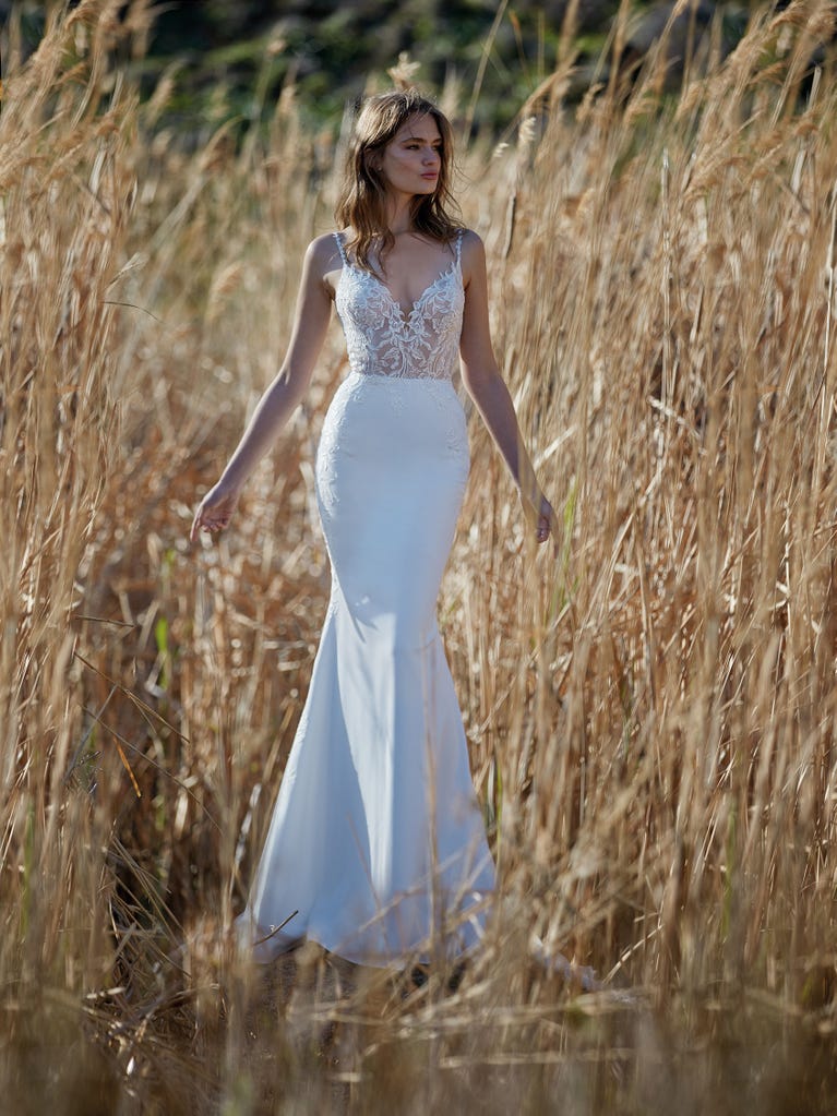 Flared wedding dress with crepe skirt and a tulle cape embroidered with silver beads. The three-dimensional flowers and minimalist, geometric superimpositions of fabrics create a contemporary, unique look for brides who want to surprise.