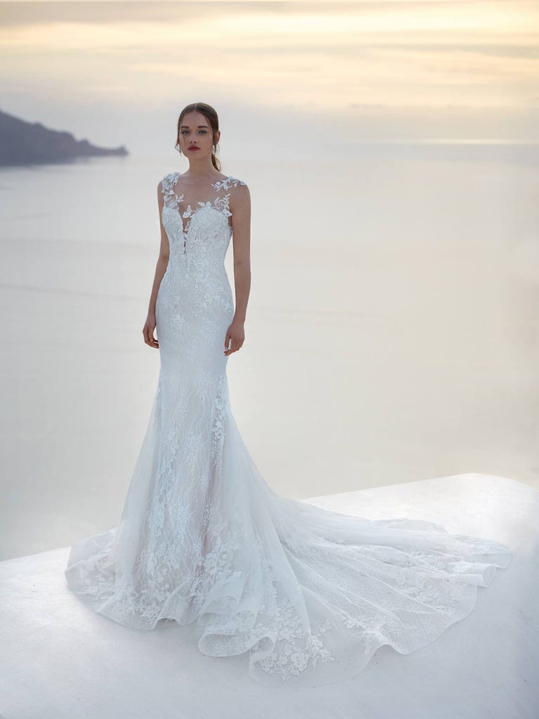 Flared wedding dress with crepe skirt and a tulle cape embroidered with silver beads. The three-dimensional flowers and minimalist, geometric superimpositions of fabrics create a contemporary, unique look for brides who want to surprise.
