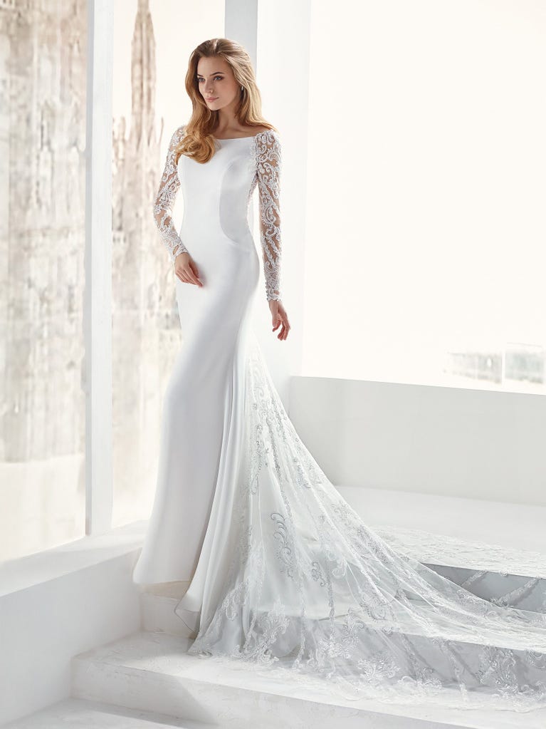 Flared wedding dress with crepe skirt and a tulle cape embroidered with silver beads. The three-dimensional flowers and minimalist, geometric superimpositions of fabrics create a contemporary, unique look for brides who want to surprise.