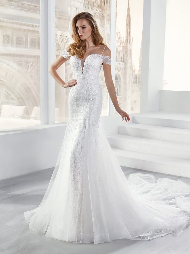 Flared wedding dress with crepe skirt and a tulle cape embroidered with silver beads. The three-dimensional flowers and minimalist, geometric superimpositions of fabrics create a contemporary, unique look for brides who want to surprise.
