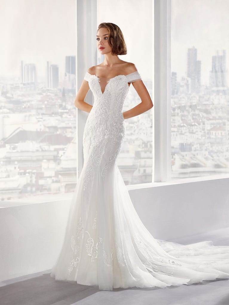 Flared wedding dress with crepe skirt and a tulle cape embroidered with silver beads. The three-dimensional flowers and minimalist, geometric superimpositions of fabrics create a contemporary, unique look for brides who want to surprise.