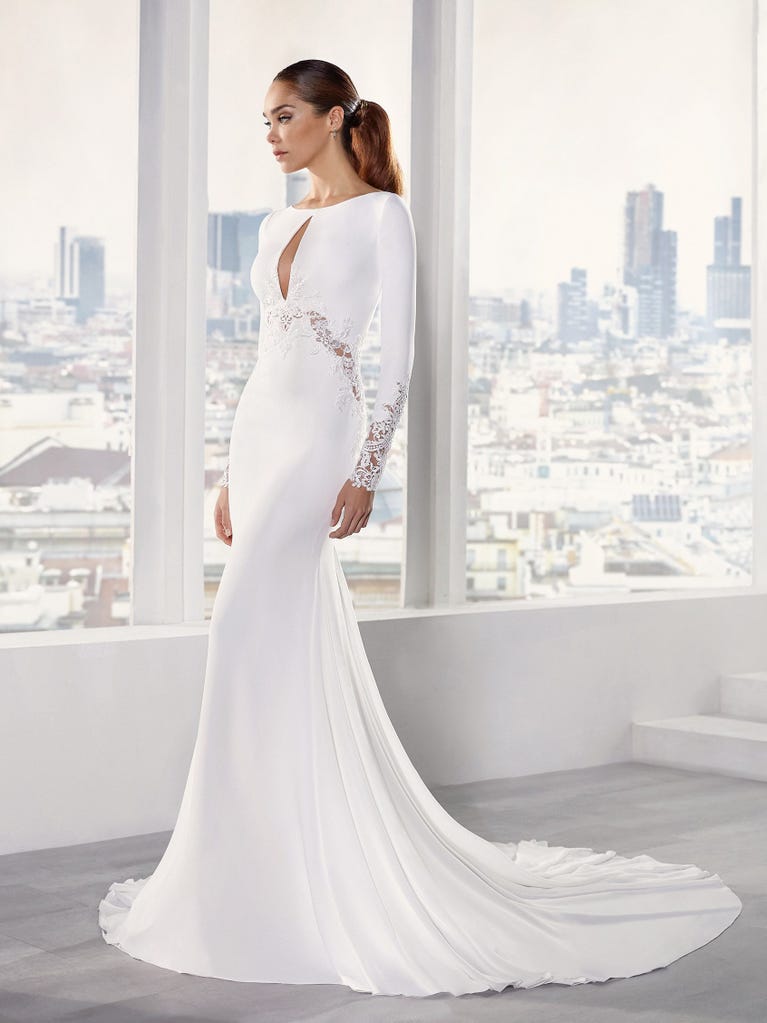 Flared wedding dress with crepe skirt and a tulle cape embroidered with silver beads. The three-dimensional flowers and minimalist, geometric superimpositions of fabrics create a contemporary, unique look for brides who want to surprise.