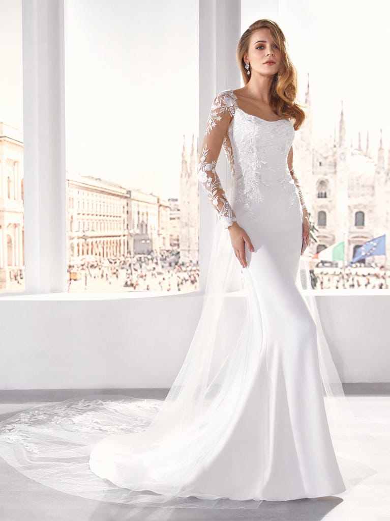 Flared wedding dress with crepe skirt and a tulle cape embroidered with silver beads. The three-dimensional flowers and minimalist, geometric superimpositions of fabrics create a contemporary, unique look for brides who want to surprise.