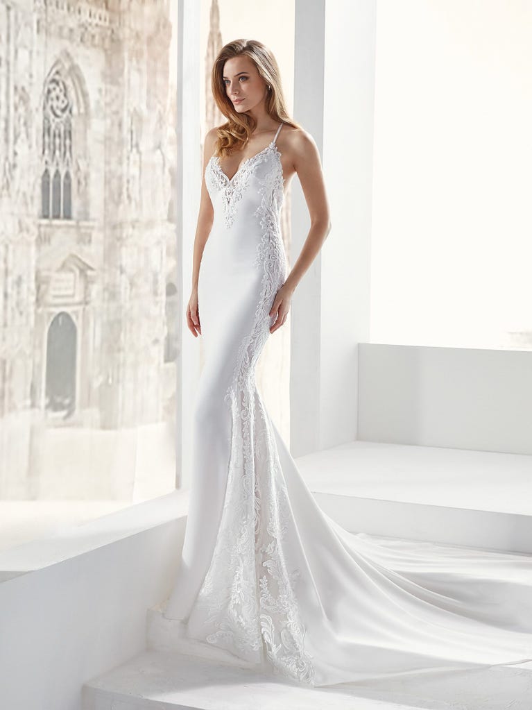 Flared wedding dress with crepe skirt and a tulle cape embroidered with silver beads. The three-dimensional flowers and minimalist, geometric superimpositions of fabrics create a contemporary, unique look for brides who want to surprise.