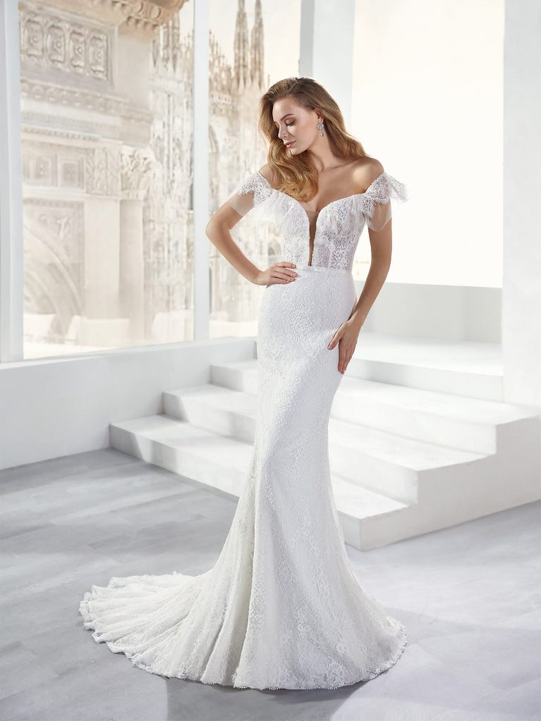 Flared wedding dress with crepe skirt and a tulle cape embroidered with silver beads. The three-dimensional flowers and minimalist, geometric superimpositions of fabrics create a contemporary, unique look for brides who want to surprise.