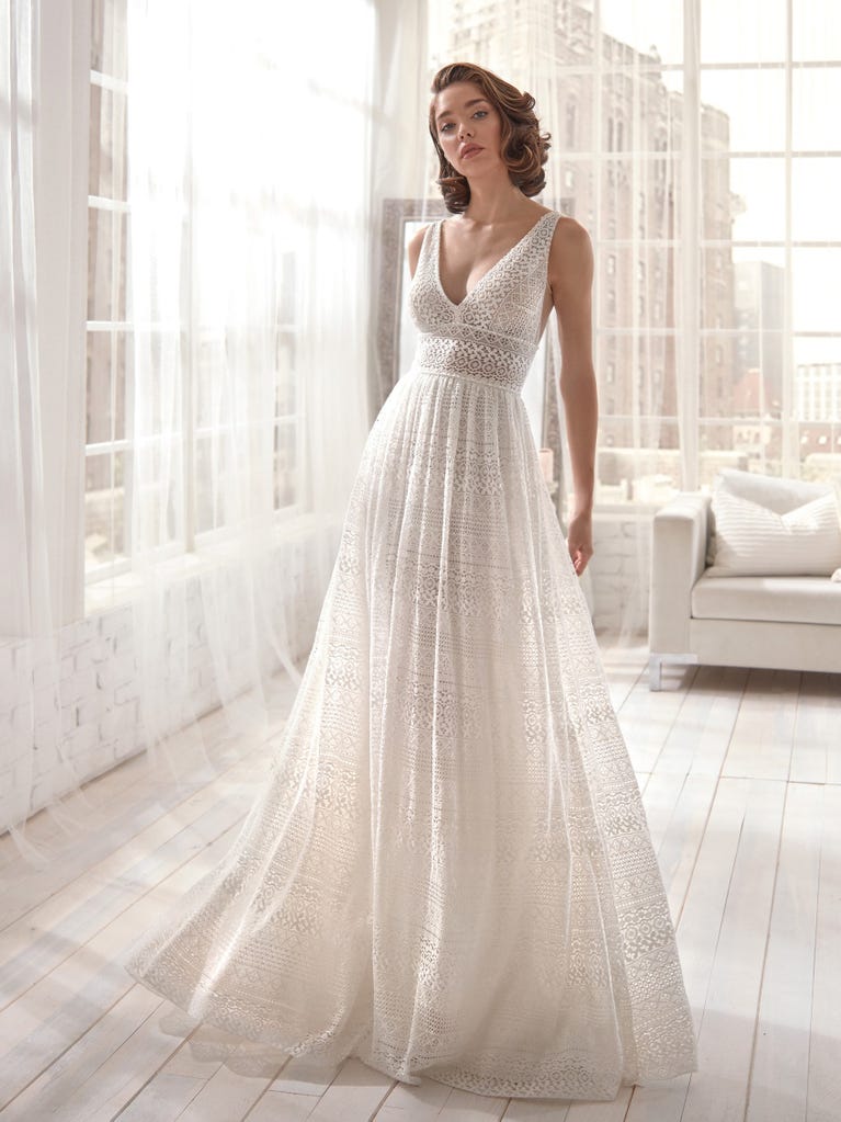 Romantic mermaid wedding dress of light pink Chantilly lace with plunging V-neck that continues on the sleeves. The keyhole opening in back and the tulle overskirt add romanticism to this dreamy dress.