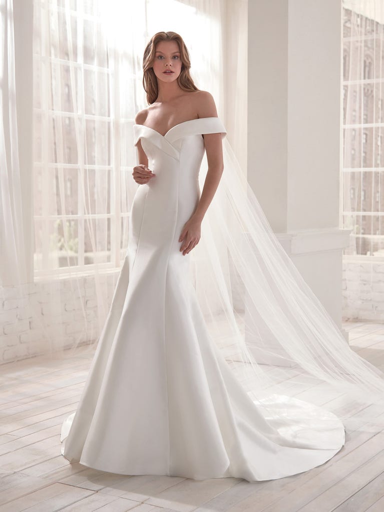 Romantic mermaid wedding dress of light pink Chantilly lace with plunging V-neck that continues on the sleeves. The keyhole opening in back and the tulle overskirt add romanticism to this dreamy dress.