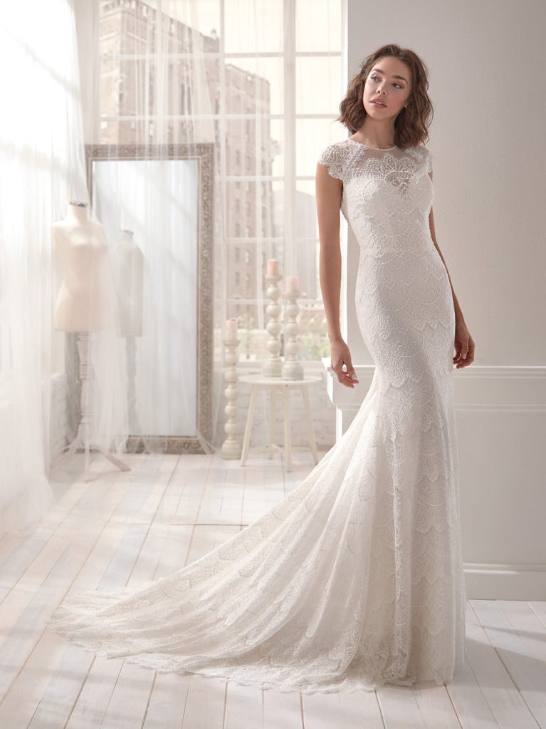 Romantic mermaid wedding dress of light pink Chantilly lace with plunging V-neck that continues on the sleeves. The keyhole opening in back and the tulle overskirt add romanticism to this dreamy dress.