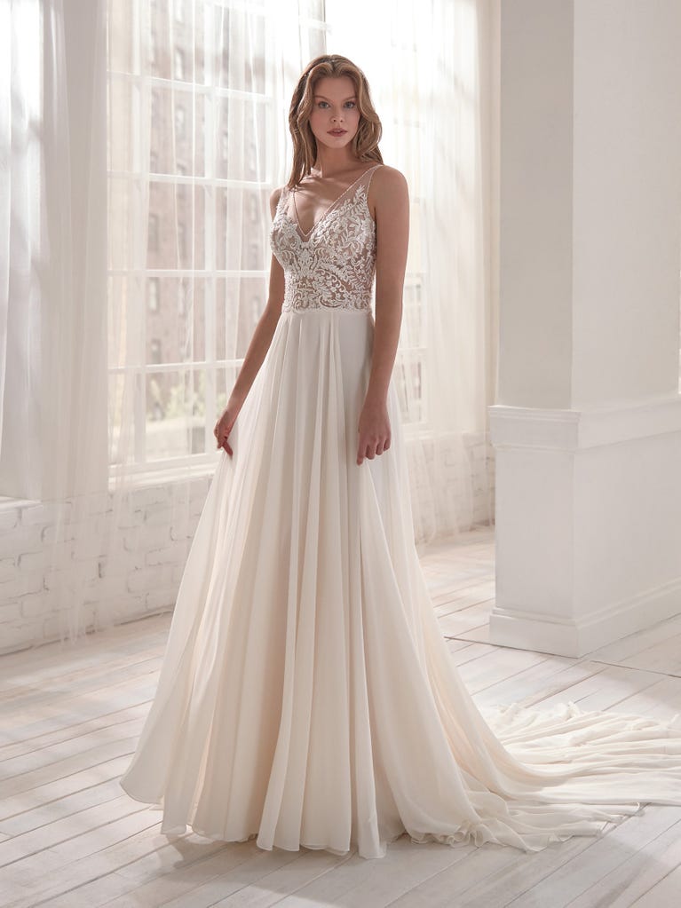 Romantic mermaid wedding dress of light pink Chantilly lace with plunging V-neck that continues on the sleeves. The keyhole opening in back and the tulle overskirt add romanticism to this dreamy dress.