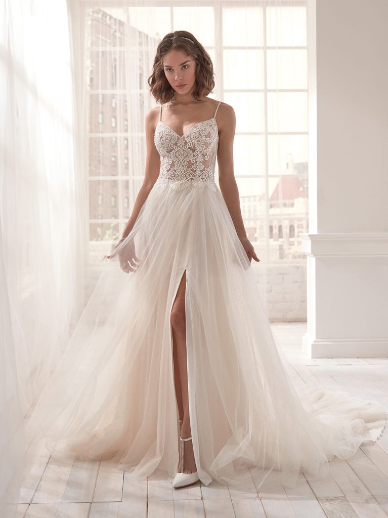Romantic mermaid wedding dress of light pink Chantilly lace with plunging V-neck that continues on the sleeves. The keyhole opening in back and the tulle overskirt add romanticism to this dreamy dress.