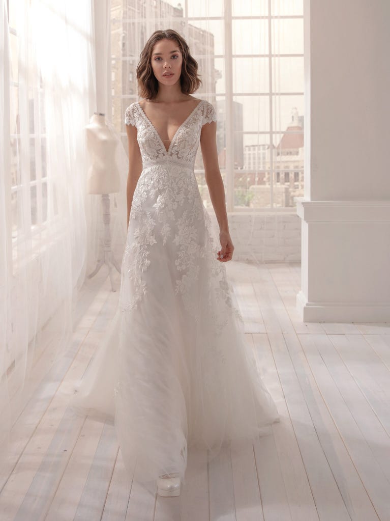 Romantic mermaid wedding dress of light pink Chantilly lace with plunging V-neck that continues on the sleeves. The keyhole opening in back and the tulle overskirt add romanticism to this dreamy dress.