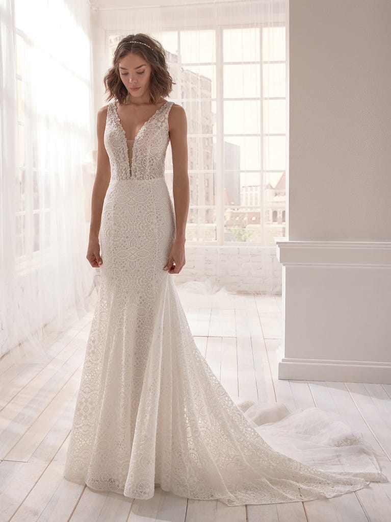 Romantic mermaid wedding dress of light pink Chantilly lace with plunging V-neck that continues on the sleeves. The keyhole opening in back and the tulle overskirt add romanticism to this dreamy dress.