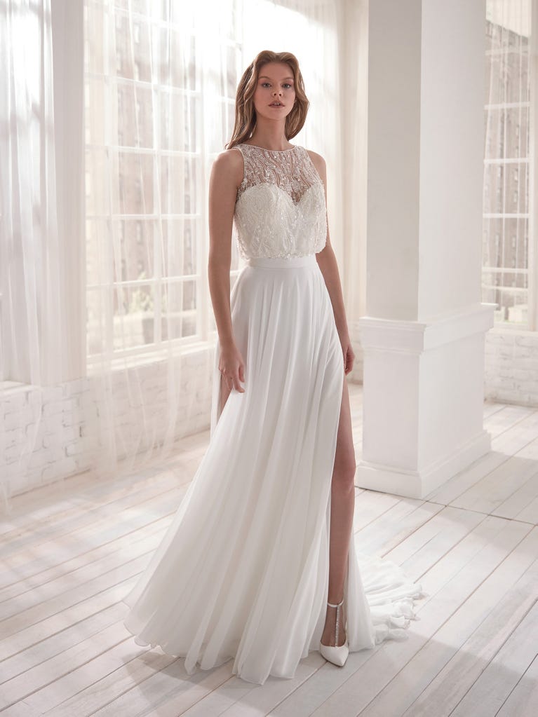Romantic mermaid wedding dress of light pink Chantilly lace with plunging V-neck that continues on the sleeves. The keyhole opening in back and the tulle overskirt add romanticism to this dreamy dress.