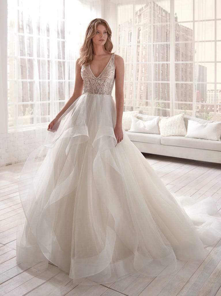 Romantic mermaid wedding dress of light pink Chantilly lace with plunging V-neck that continues on the sleeves. The keyhole opening in back and the tulle overskirt add romanticism to this dreamy dress.