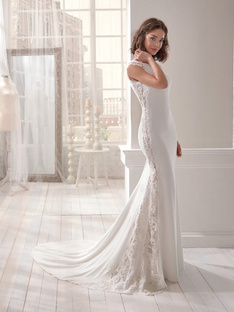 Romantic mermaid wedding dress of light pink Chantilly lace with plunging V-neck that continues on the sleeves. The keyhole opening in back and the tulle overskirt add romanticism to this dreamy dress.