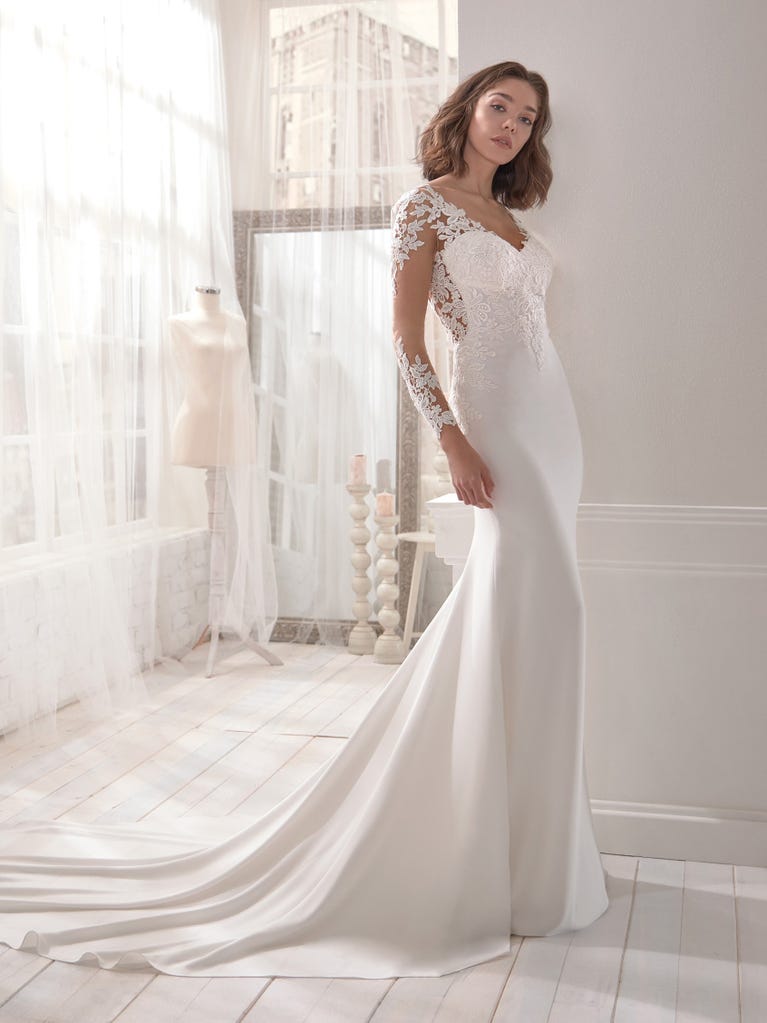 Romantic mermaid wedding dress of light pink Chantilly lace with plunging V-neck that continues on the sleeves. The keyhole opening in back and the tulle overskirt add romanticism to this dreamy dress.
