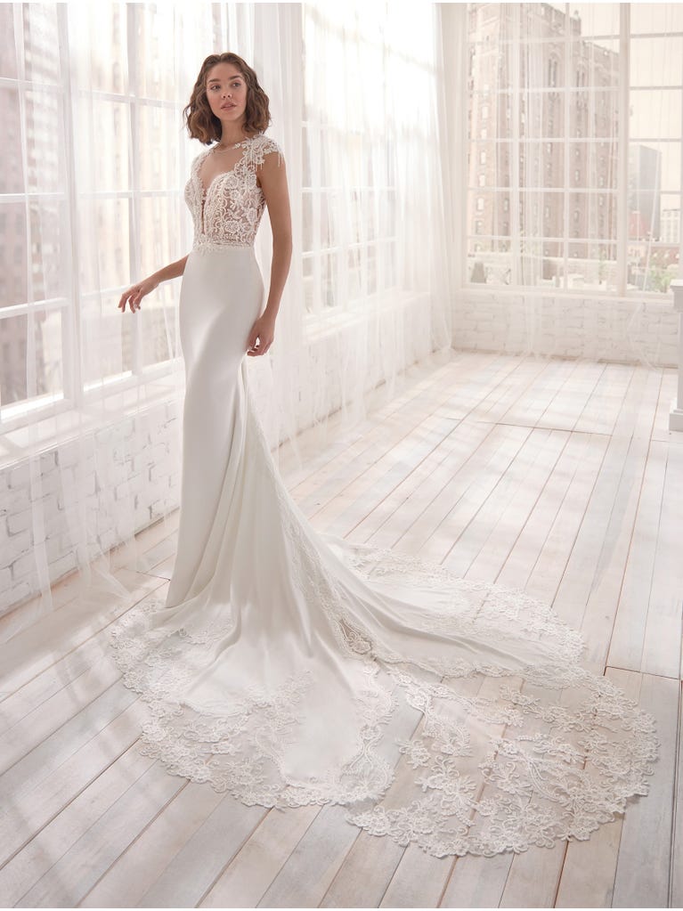 Romantic mermaid wedding dress of light pink Chantilly lace with plunging V-neck that continues on the sleeves. The keyhole opening in back and the tulle overskirt add romanticism to this dreamy dress.