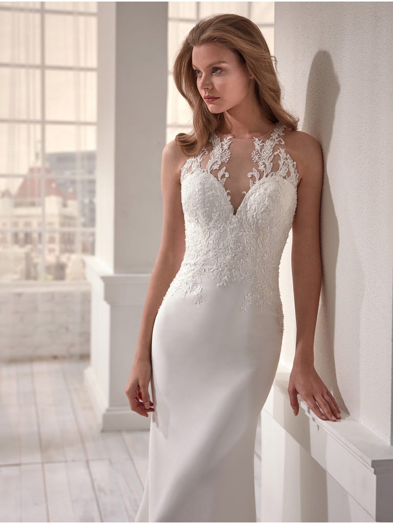 Romantic mermaid wedding dress of light pink Chantilly lace with plunging V-neck that continues on the sleeves. The keyhole opening in back and the tulle overskirt add romanticism to this dreamy dress.