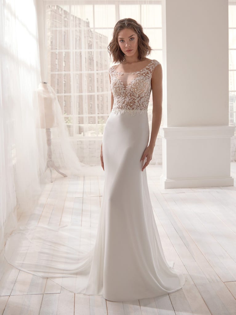 Romantic mermaid wedding dress of light pink Chantilly lace with plunging V-neck that continues on the sleeves. The keyhole opening in back and the tulle overskirt add romanticism to this dreamy dress.