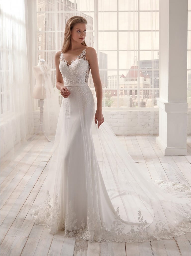 Romantic mermaid wedding dress of light pink Chantilly lace with plunging V-neck that continues on the sleeves. The keyhole opening in back and the tulle overskirt add romanticism to this dreamy dress.