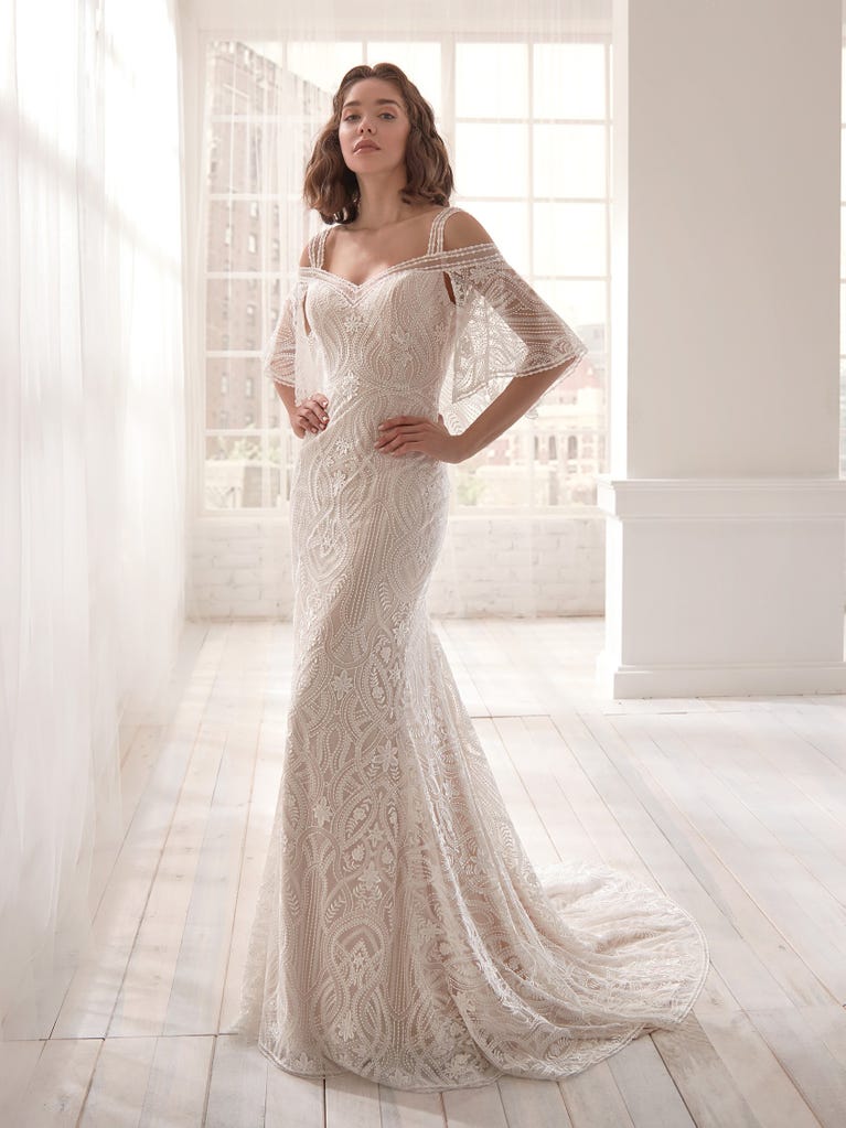 Romantic mermaid wedding dress of light pink Chantilly lace with plunging V-neck that continues on the sleeves. The keyhole opening in back and the tulle overskirt add romanticism to this dreamy dress.