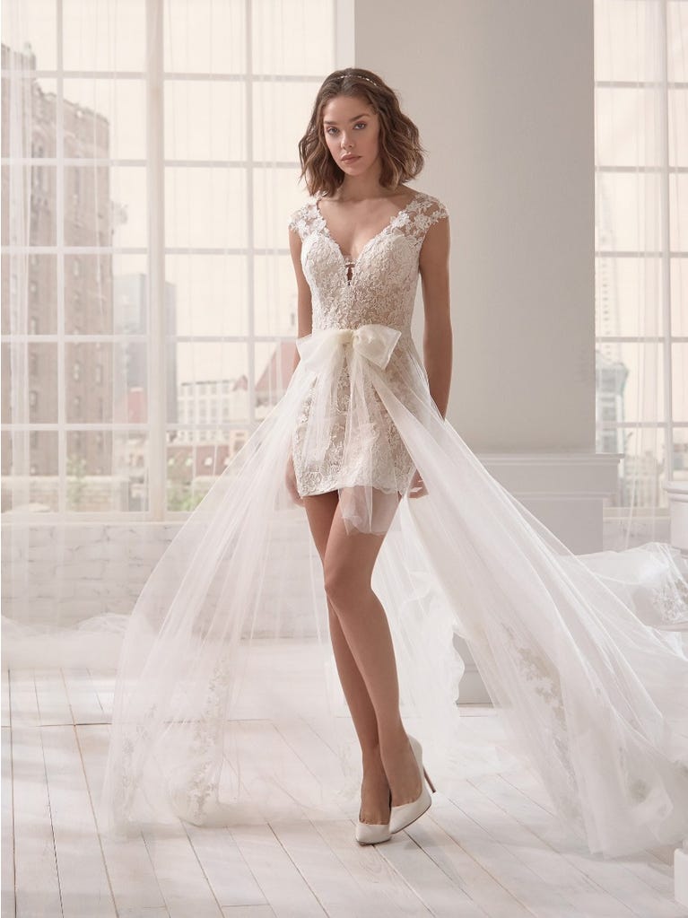 Romantic mermaid wedding dress of light pink Chantilly lace with plunging V-neck that continues on the sleeves. The keyhole opening in back and the tulle overskirt add romanticism to this dreamy dress.